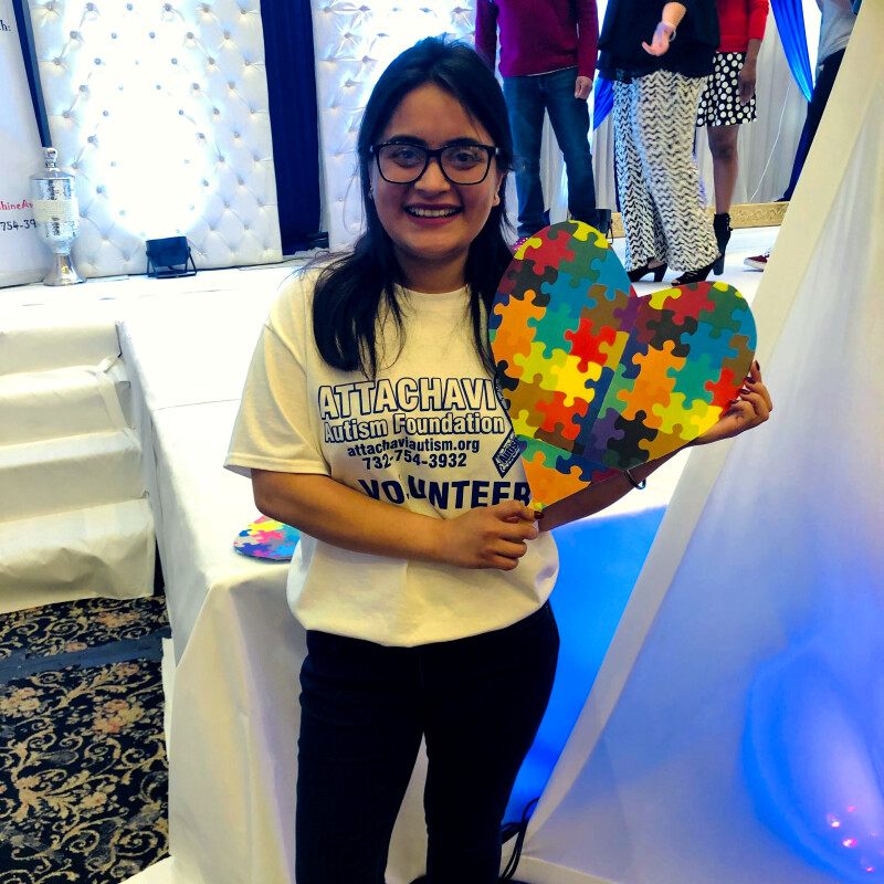 Woman holding a heart made of puzzle pieces in front of a stage.