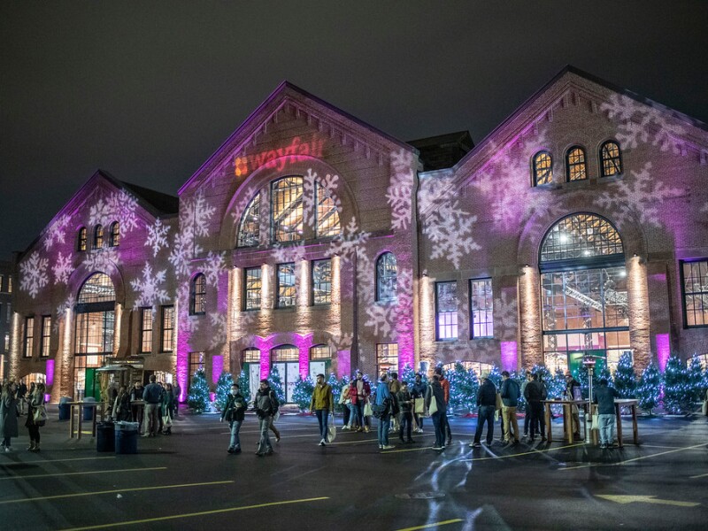 A look at the SoWa market building, which has snowflake images projected onto it, as the festive building looms over a crowd of people.