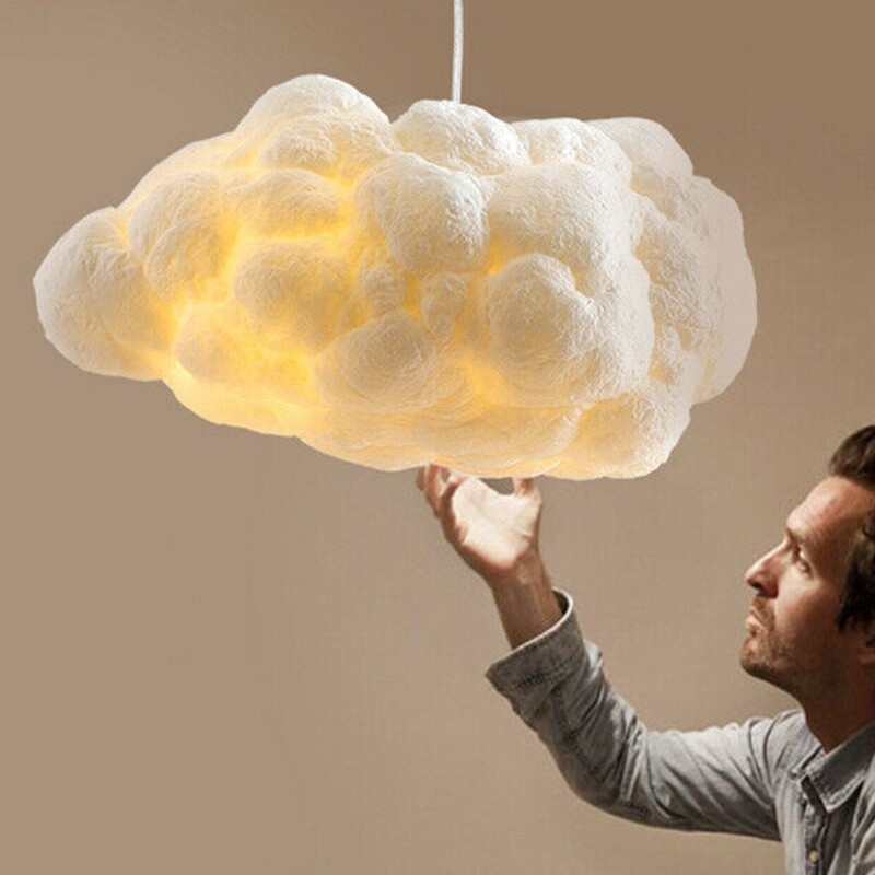 A white and fluffy lamp in the shape of a cloud hangs on a single string; a man leans forward to inspect it.