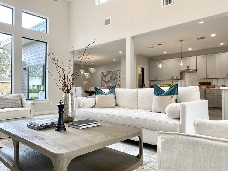 An all-white living room with a gray table, a white couch, and white pillows with blue accents.