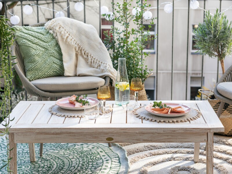 Two plates are set and ready for food on a light tan table in the sunlight.