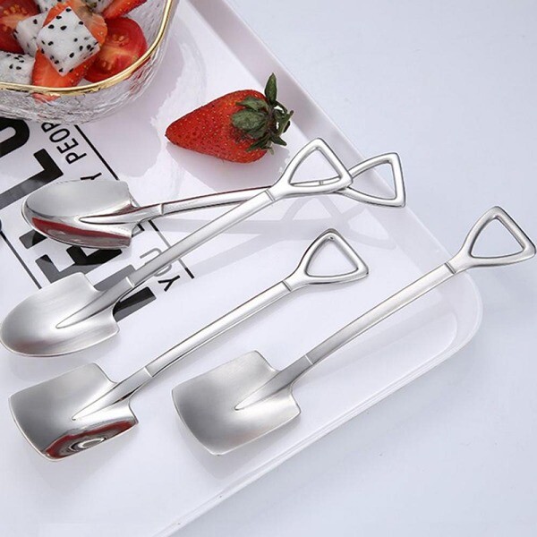 Silver, shovel-shaped small spoons on a plate with strawberries.