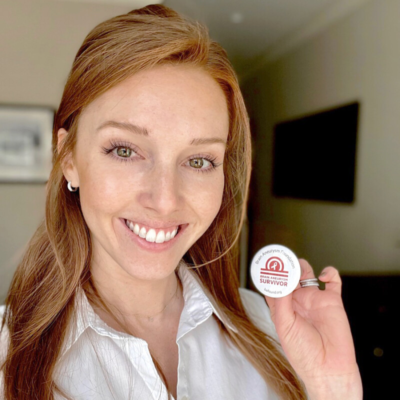 Woman holding a pin that says "Brain Aneurysm Survivor"