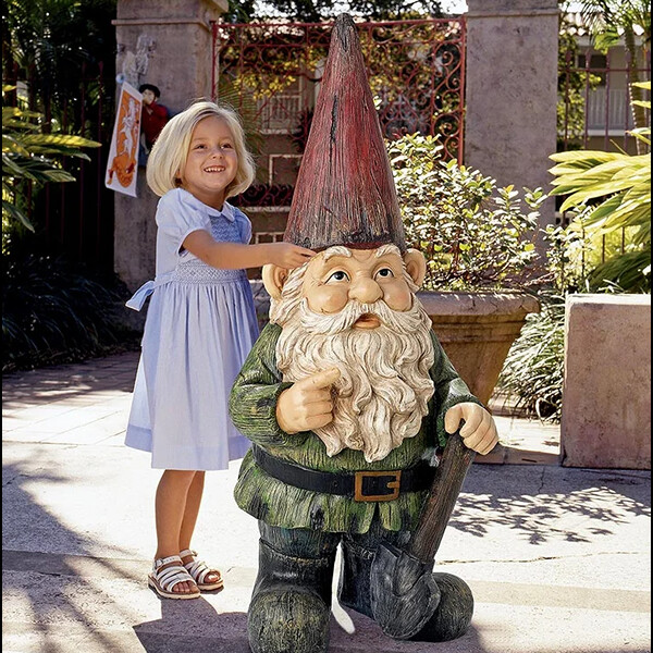 Child in blue dress standing next to child-size ceramic garden gnome.