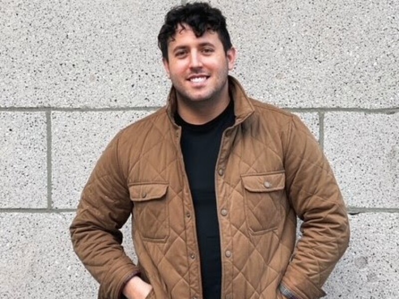 Wayfair Recruiter Anthony Gutierrez stands with a smile in front of a stone wall.